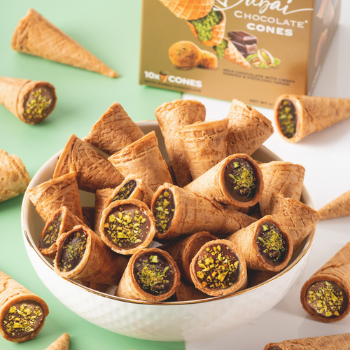 Pistachio-filled chocolate cones in a bowl with a box of the product in the background.